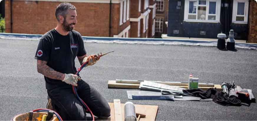 A sole trader checks their tools before continuing with a flat-roofing job